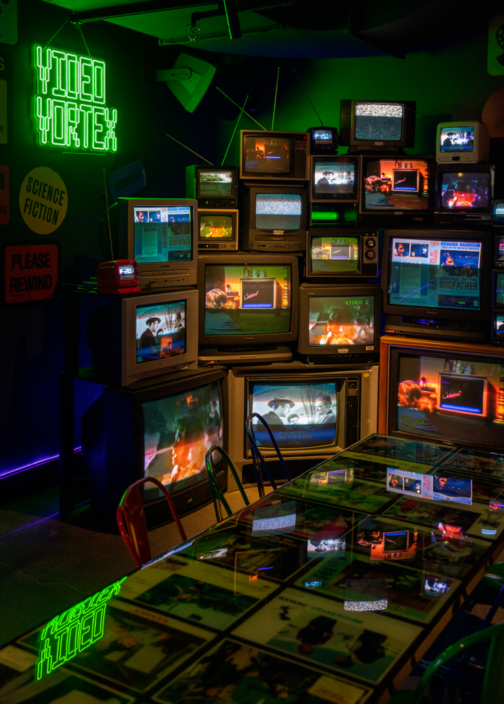 Video Vortex dining area, filled with crt and transistor tvs, all playing displaying different films.